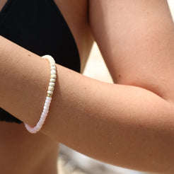 A close-up of a person's forearm wearing a beaded bracelet made of small white and pale pink beads with a tiny gold accent.